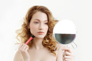 A young woman looking into the mirror while applying makeup
